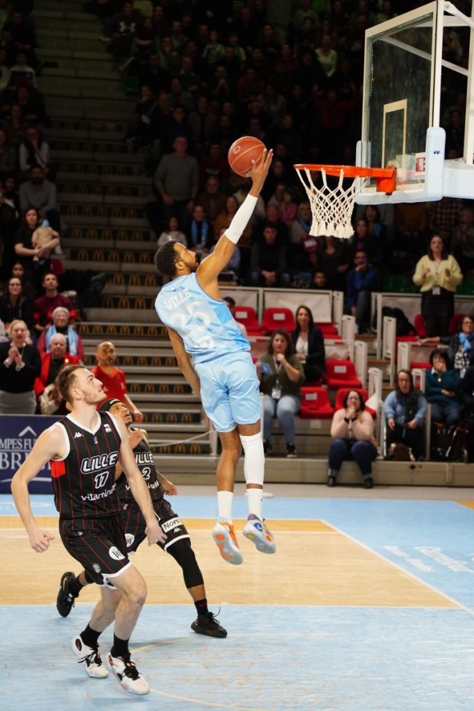 Activités : Joueur de basket en sautant au dessous du panier pour mettre un panier durant un match de la JAV en 2023