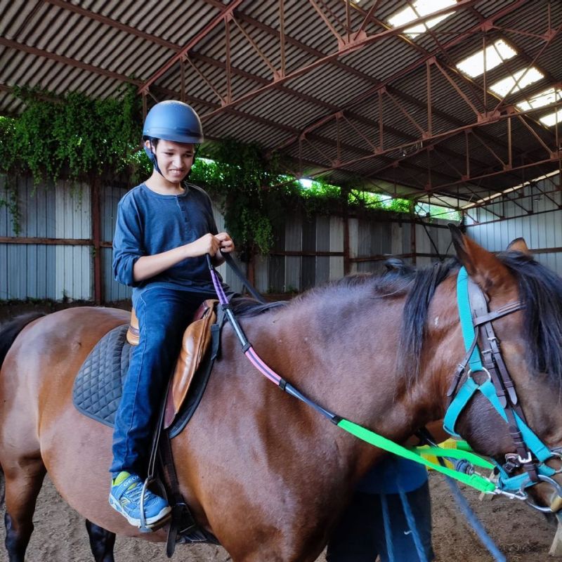 Séance équihandi : Un enfant en situation de handicap heureux d'être sur le dos d'un poney.