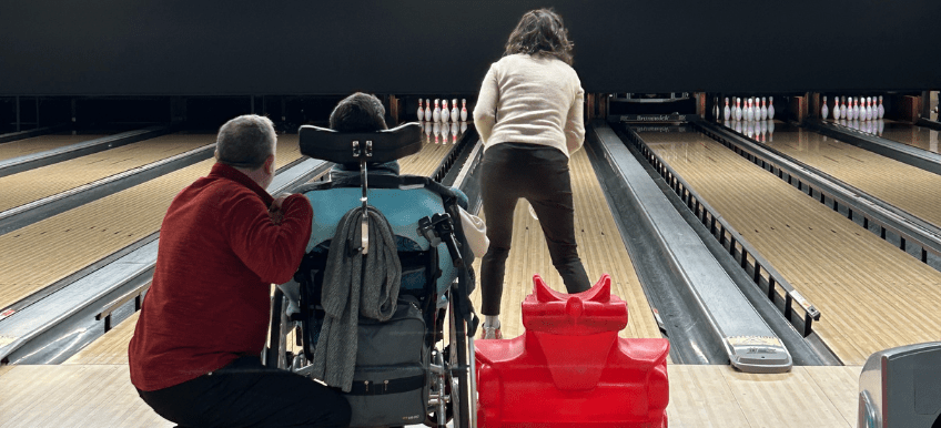 Personne en fauteuil roulant jouant avec d'autres personnes au bowling au sein du B.Bowl