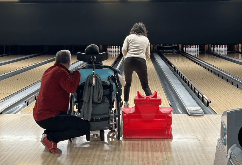 Personne en fauteuil roulant jouant avec d'autres personnes au bowling au sein du B.Bowl