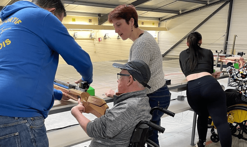 découverte du Paratir. Un coach explique et aide un homme en fauteuil manuel à réaliser l'activité