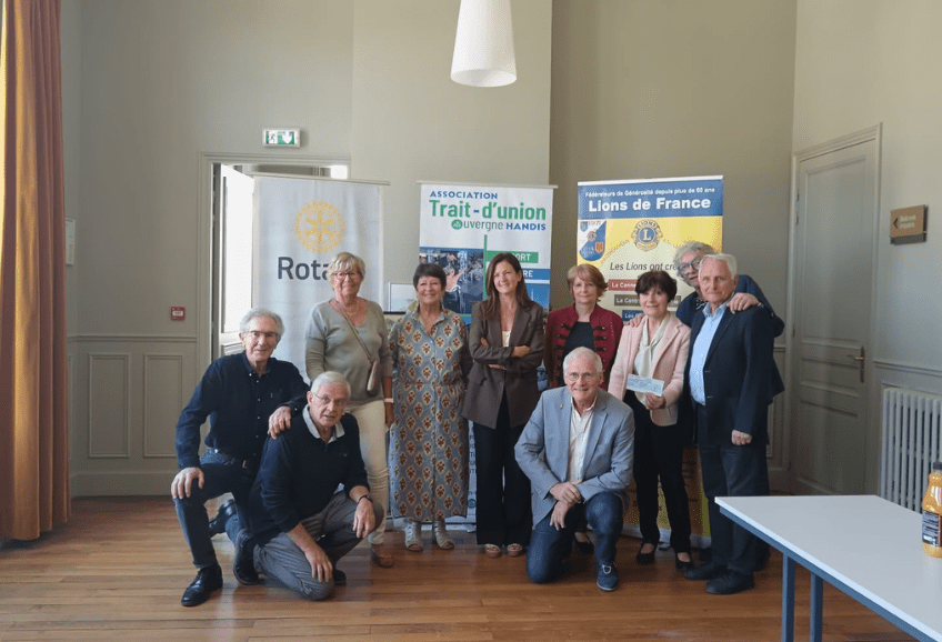 Remise du chèque du rotary club de Châtel Guignon en soutien au projet handidôme de l'Association Trait d'union Auvergne Handis. Marie directrice de la sociation est entourée de 9 personnes du rotary club. Tous sont souriant. les affiches des différentes associations Rotary , lions club et ATUAH sont derrières ces personnes.