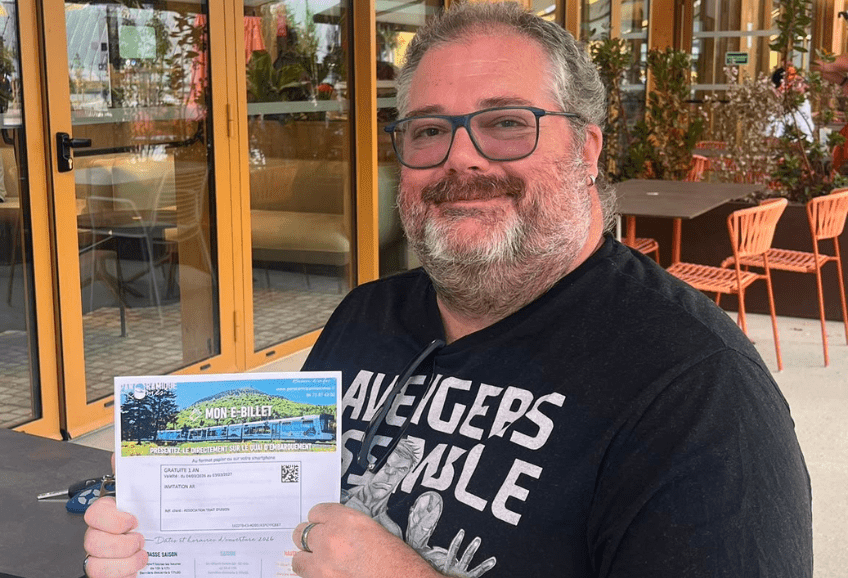 Homme souriant bénéficiaire de l'association montrant son billet pour les nocturnes du puy de dôme offert par l'association