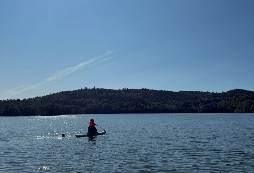 Sécurisé par Christophe dans l'eau, un participant pagaie sur le paddle adapté au milieu du lac