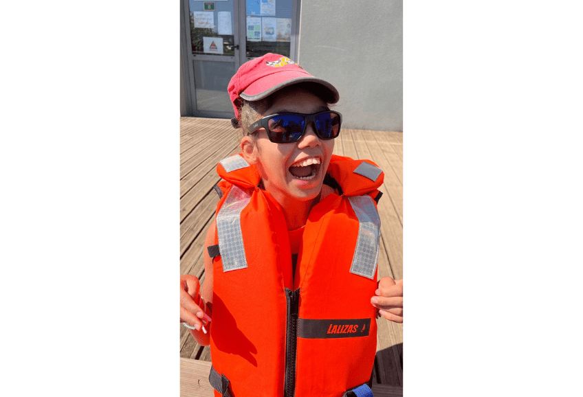 Une fille souriante avec des lunettes de soleil et une casque. Elle porte un gilet de sauvetage orange.